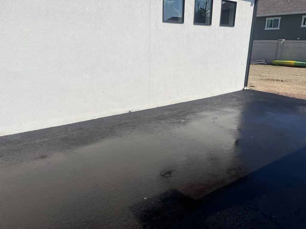 White building wall with small windows and a dark paved driveway in bright sunlight
