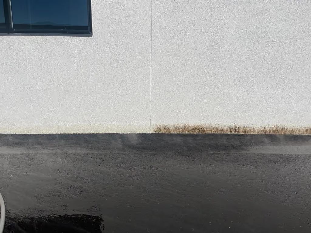 White stucco wall above dark asphalt, with a small window and a strip of dirt along the base.
