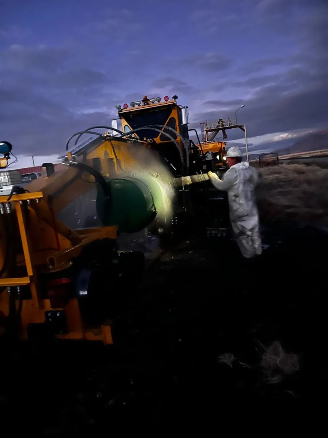 Worker in white suit inspecting a large industrial machine at dusk outdoors