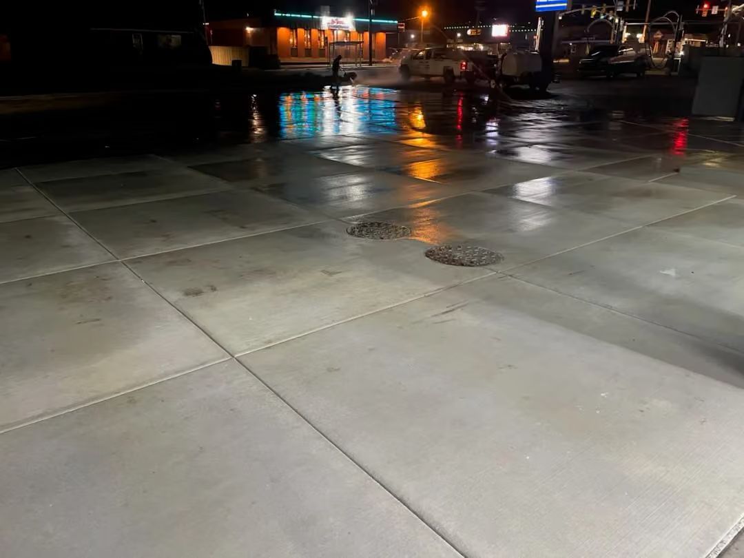 Wet concrete sidewalk at night with streetlights reflecting in the pavement and blurred cars in the background