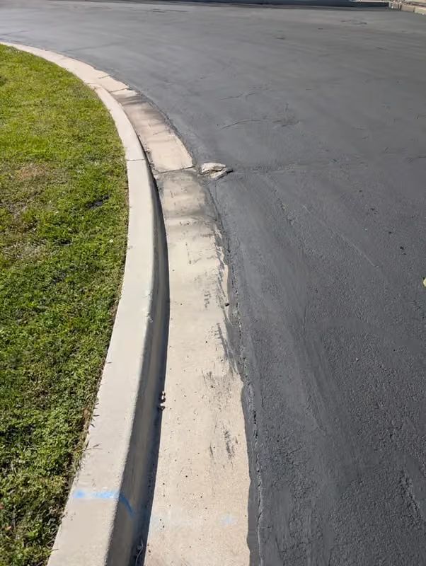 Curved asphalt road edge with a concrete curb and a strip of green grass
