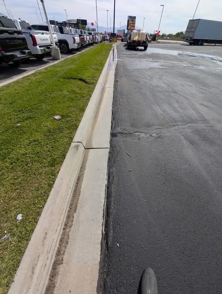 Parking lot beside curb and grassy median, with wet pavement and cars in the distance.