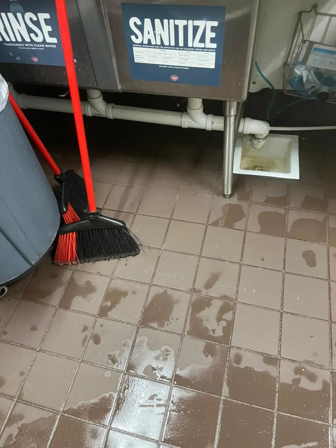 Wet tiled floor with mop and broom in front of sanitize bins and spill cleanup area
