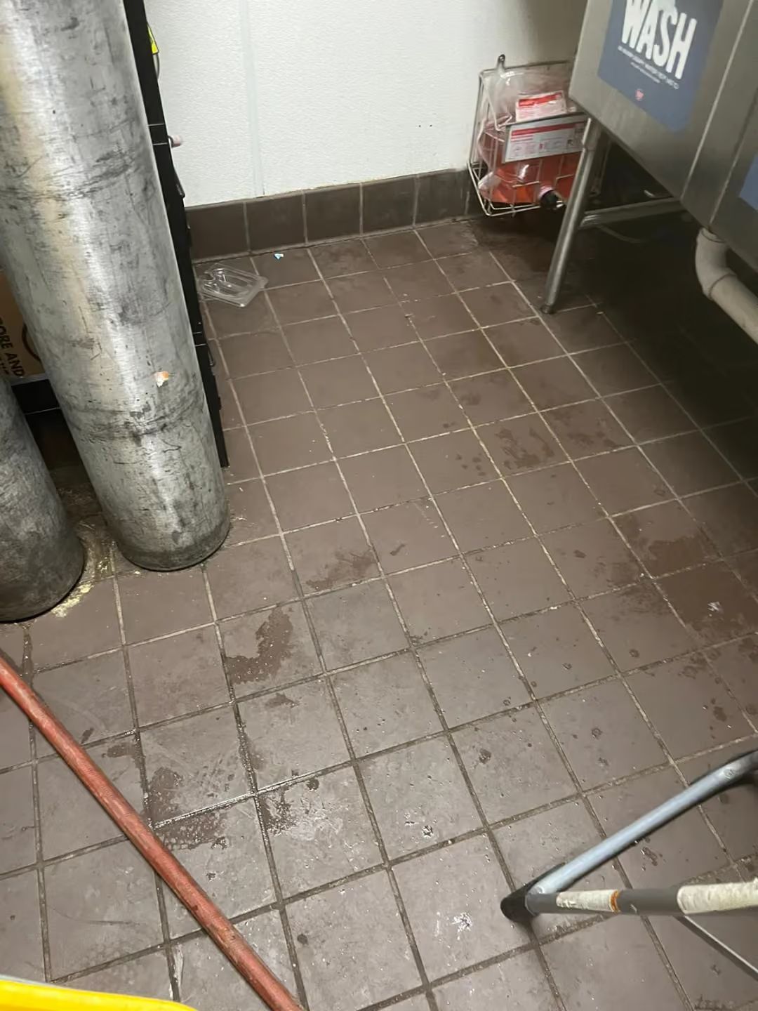Wet tiled floor beside metal tanks and a cart in a utility area