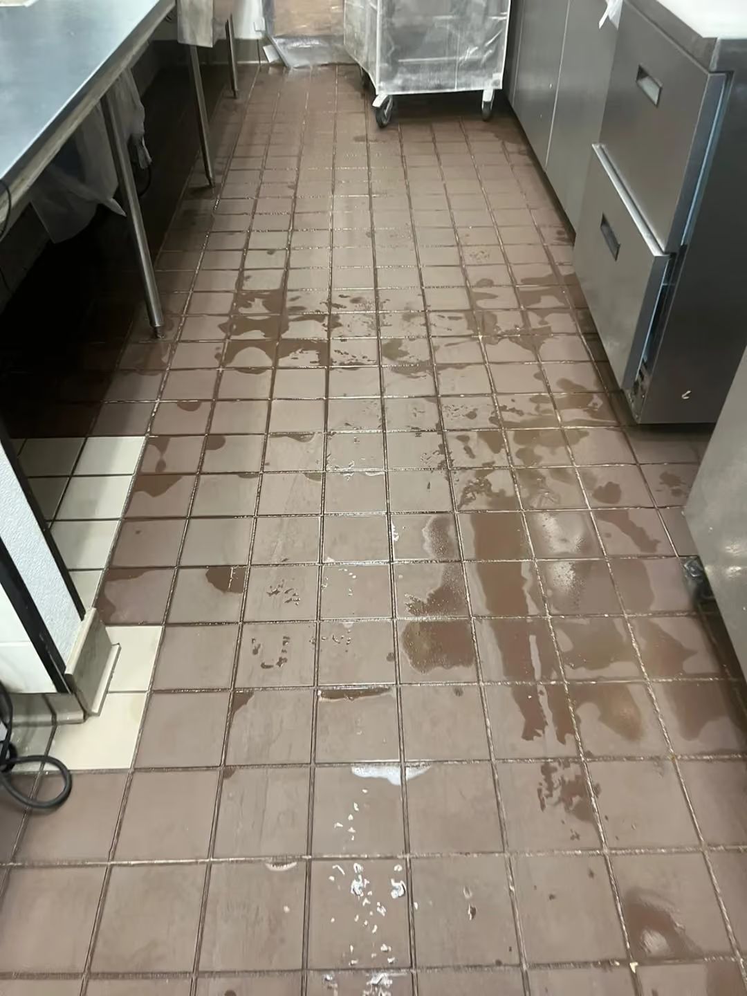 Wet tiled kitchen floor with puddles and stainless steel counters on both sides