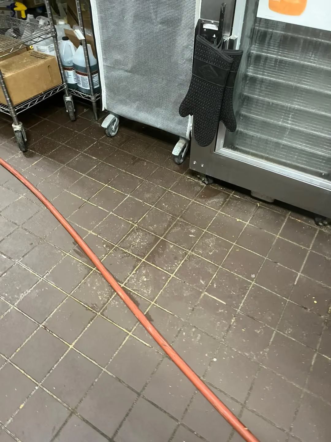 Red hose on tiled floor beside metal racks and a black appliance in a storage area
