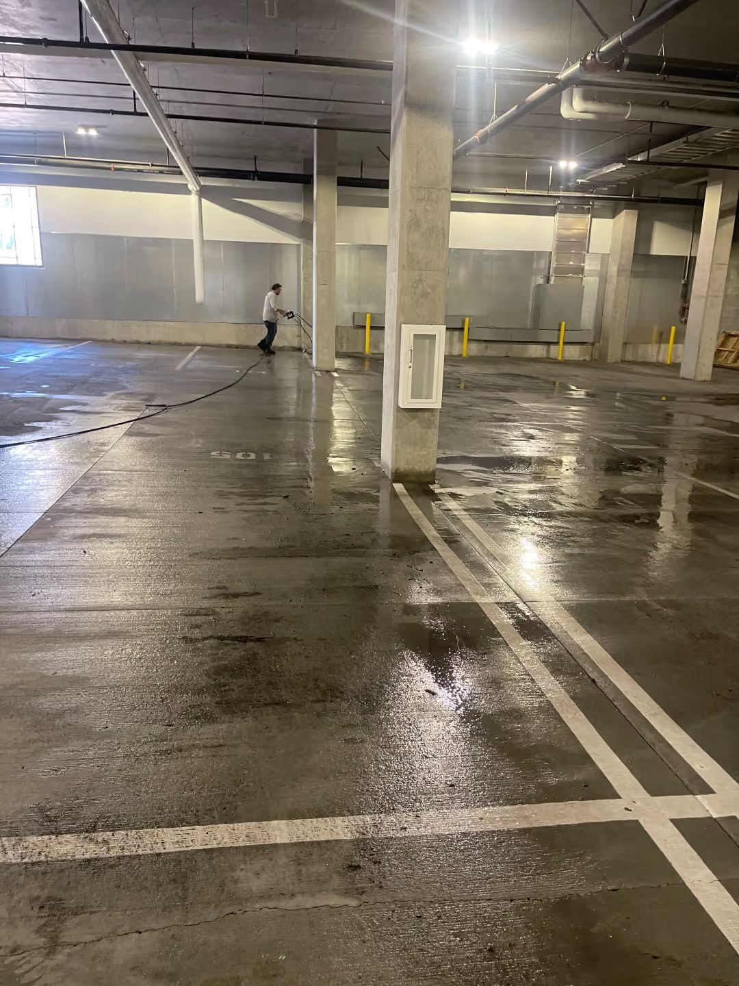 Empty wet parking garage with concrete pillars and a person walking in the distance