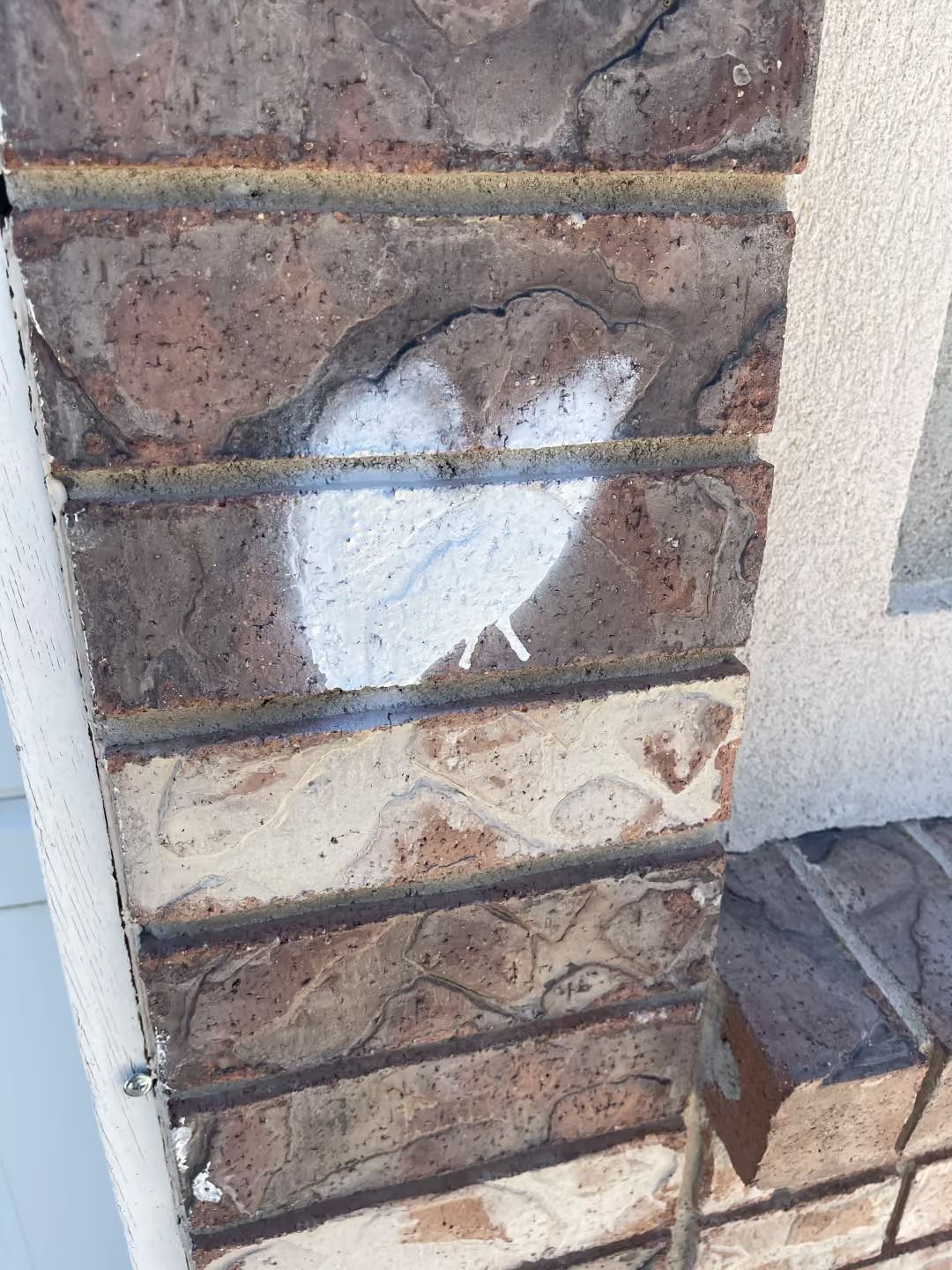 Damaged exterior brick wall with white patching and a small section of stacked bricks at the base