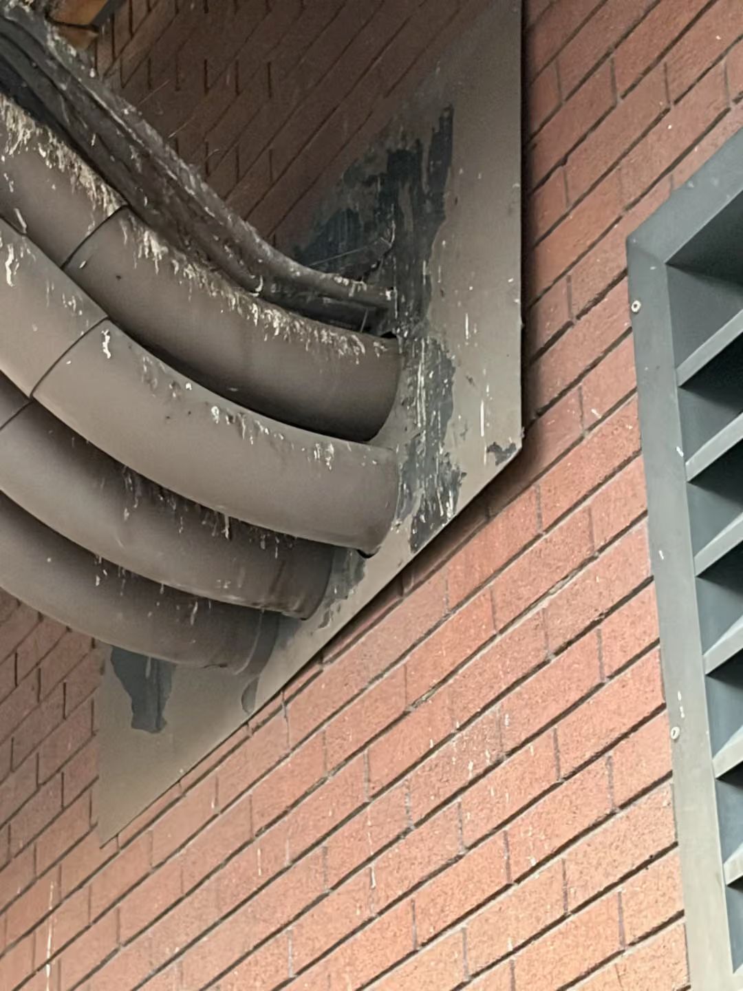 Brick wall with a damaged concrete soffit and exposed curved pipes or ducts underneath