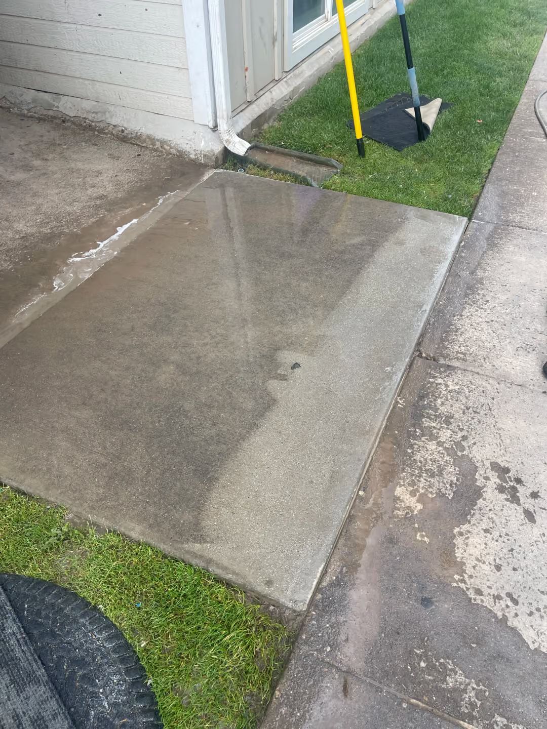 Concrete wheelchair ramp beside a doorway, with a shovel and yellow handle leaning nearby.