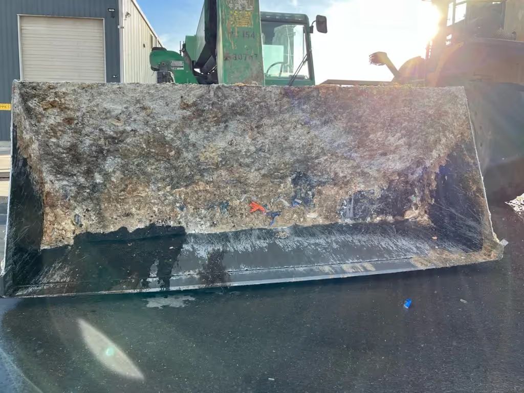 Large rusty excavator bucket dumping debris onto a wet black surface outdoors