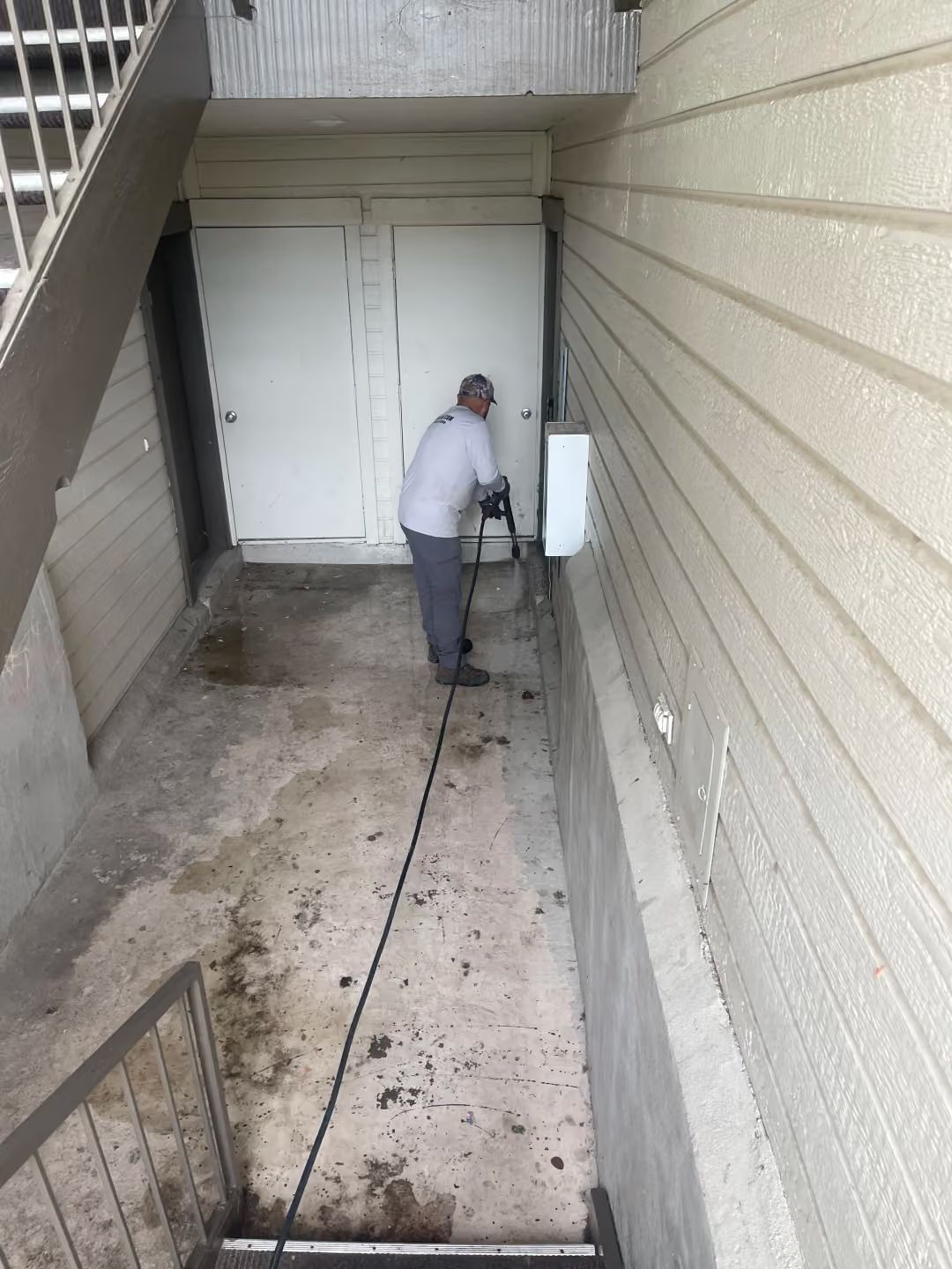 Person cleaning a concrete stairwell landing beside a white door and beige wall.