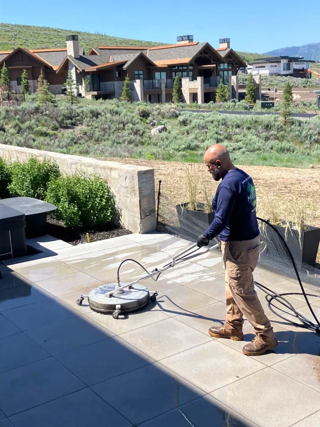 Man using a pressure washer on a patio beside a garden and house