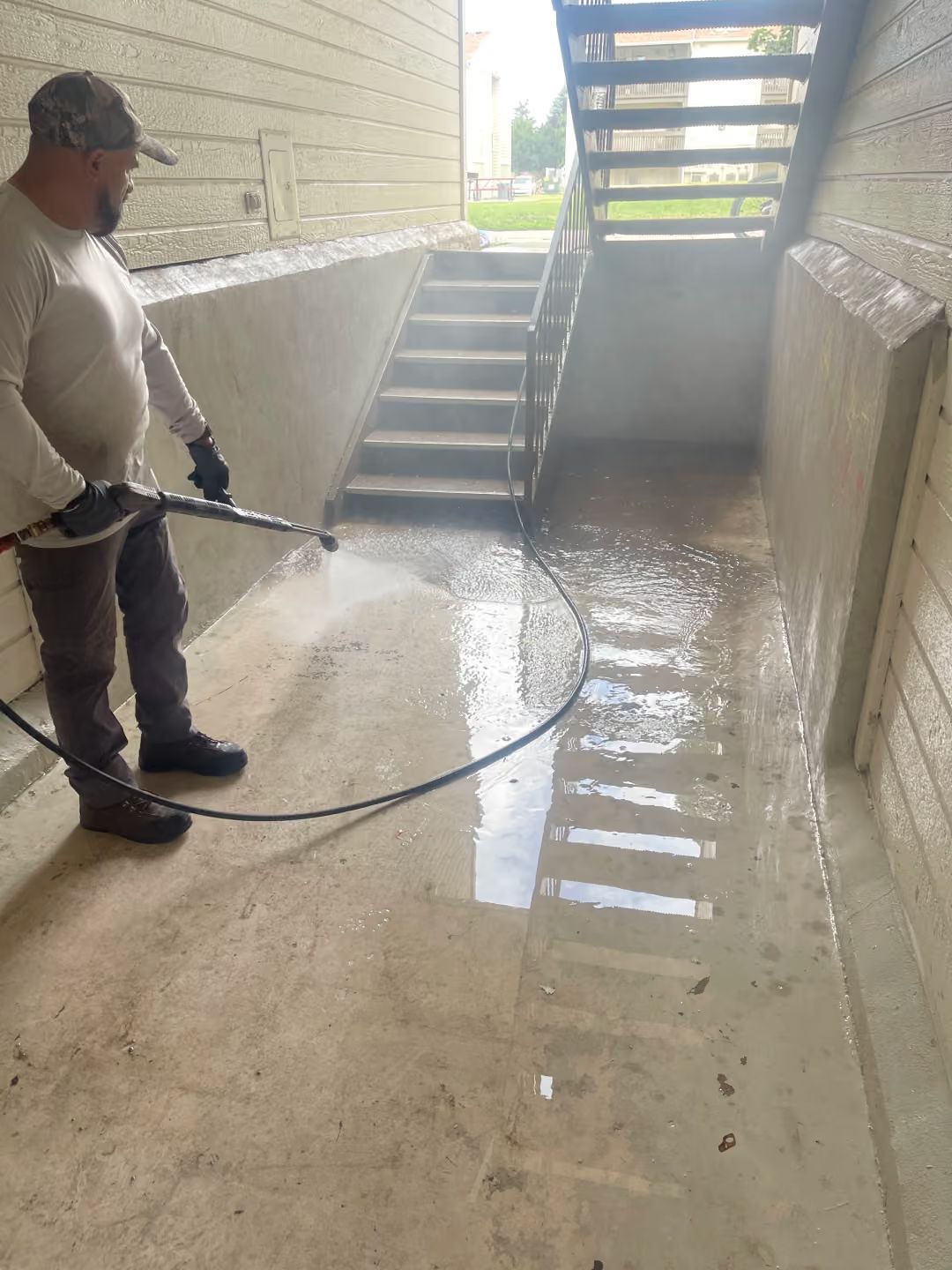 Worker power-washing a wet concrete stairwell under an overpass