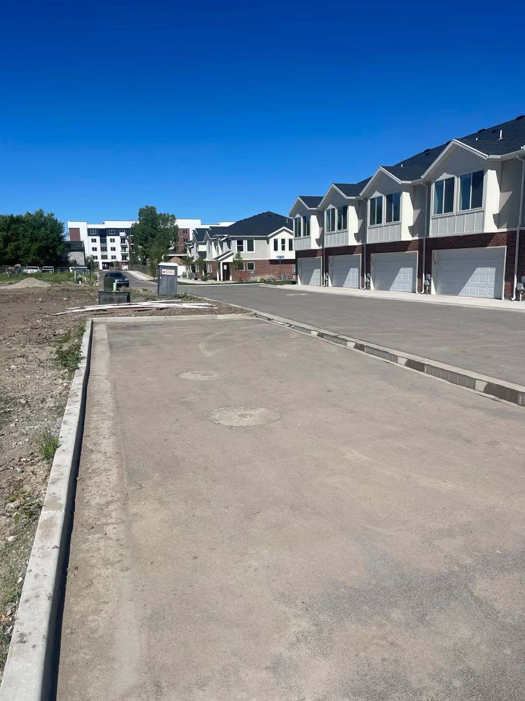 New residential street with unfinished sidewalks and rows of townhouses under a clear blue sky