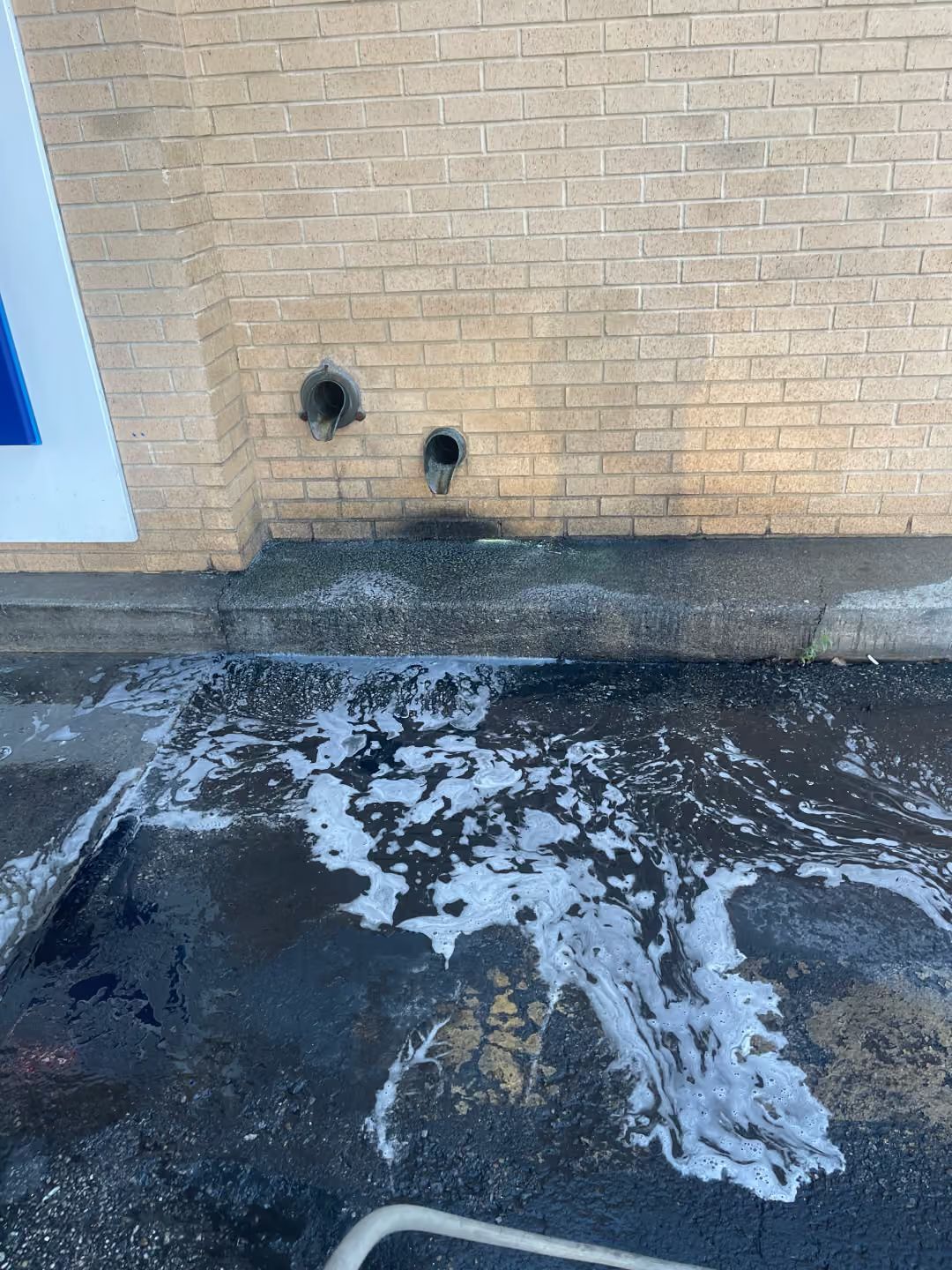 Brick building wall with two holes above a wet, slushy pavement.