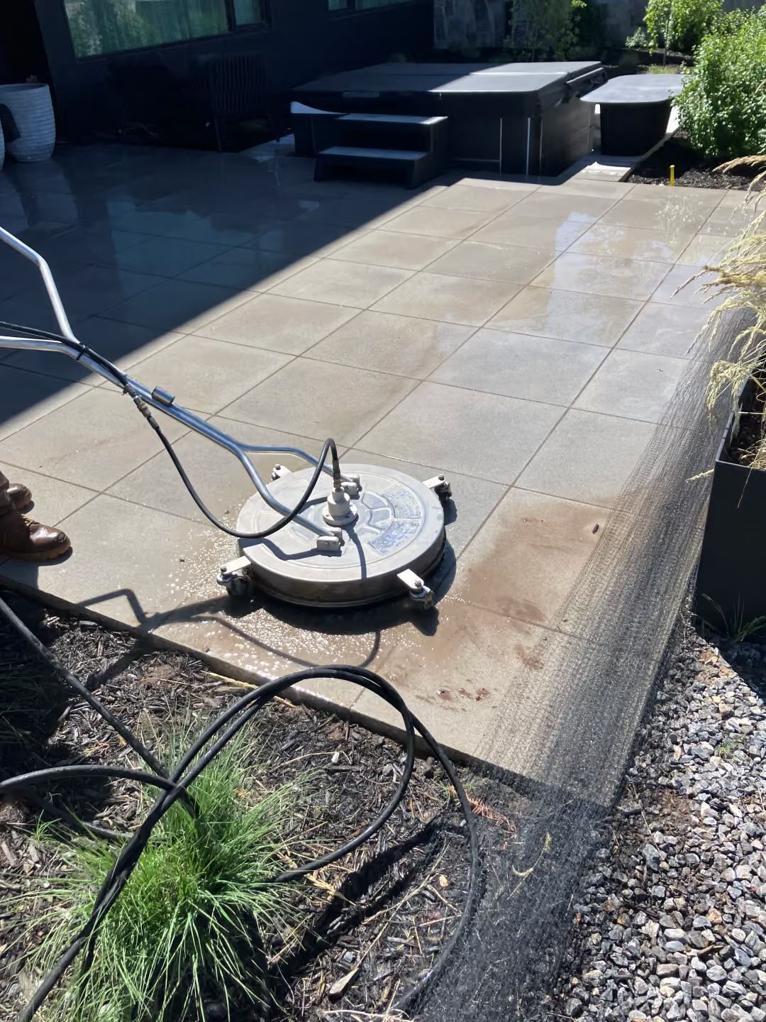Pressure washer cleaning a sunlit stone patio near a pool and outdoor seating area