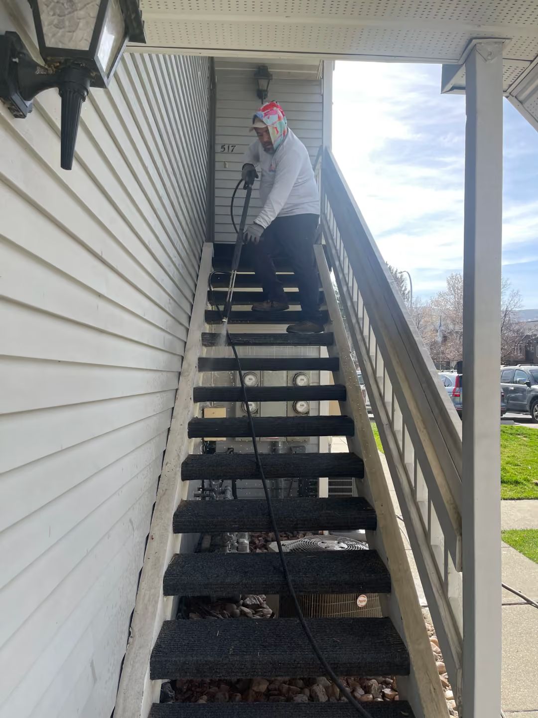Person on outdoor apartment stairs carrying a tool, with a black cable running down the steps.
