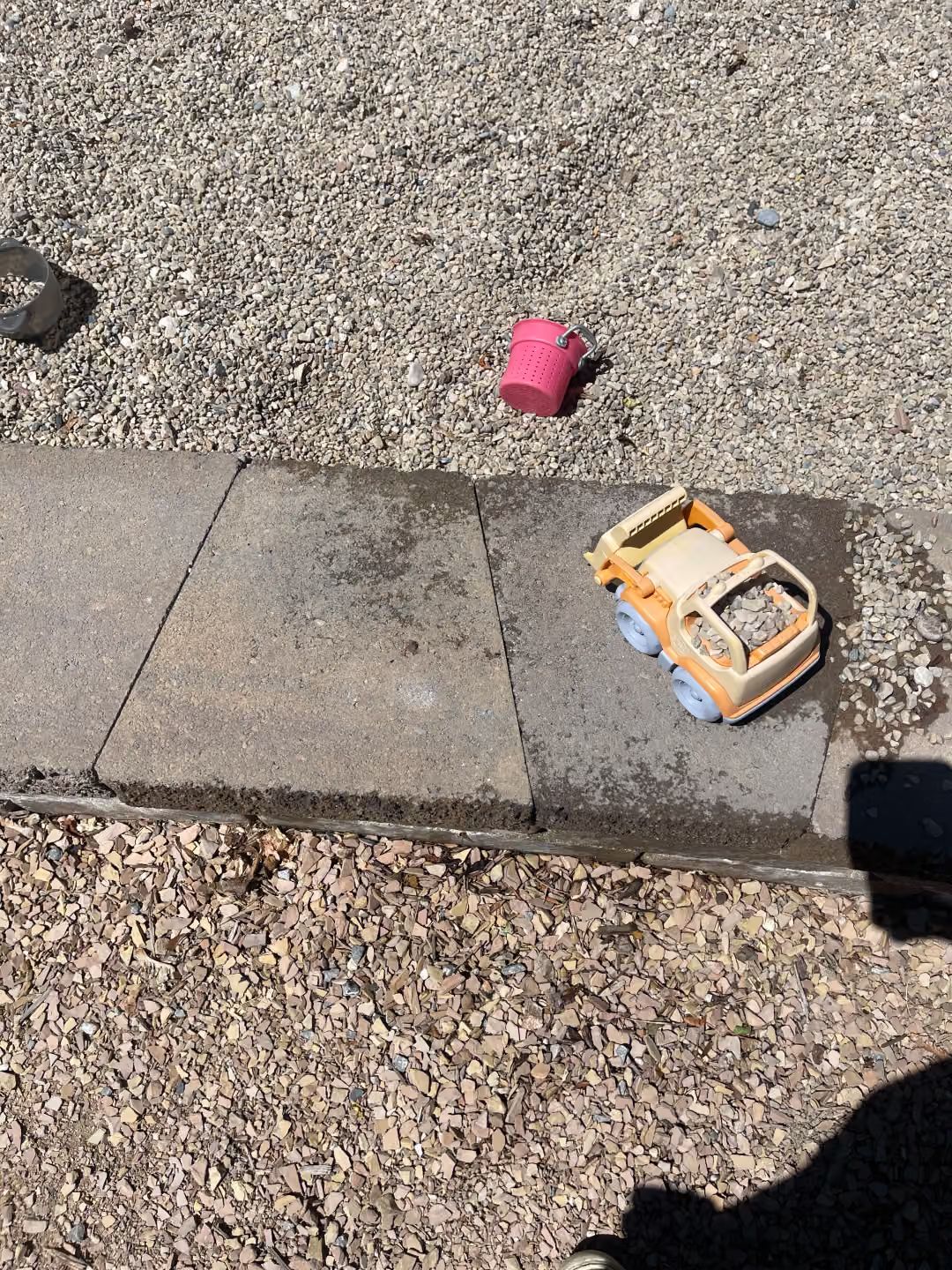 Pink cup and toy car on gravel beside a concrete curb.