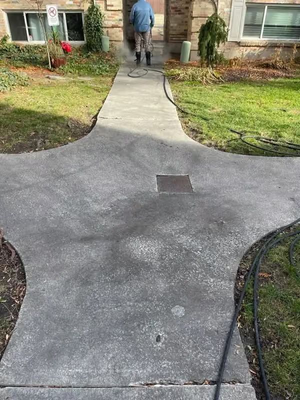 Front walkway leading to a house entrance, with a person walking away near a concrete path and lawn.