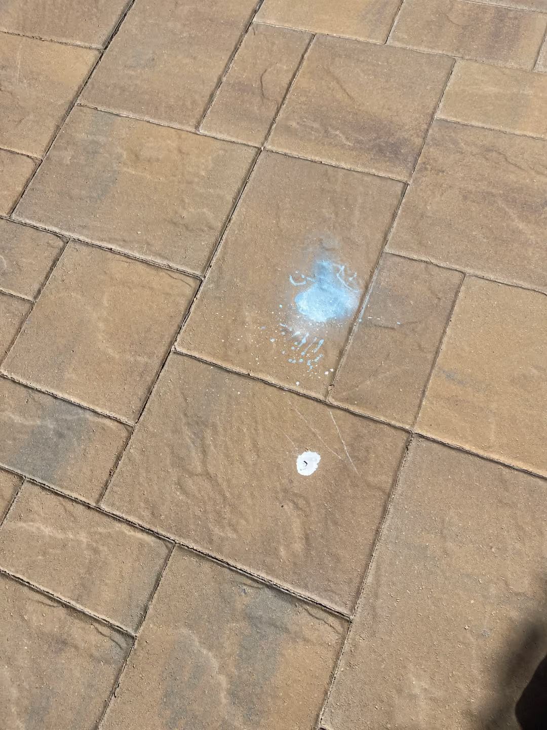 Tan brick pavement with a small blue paint mark and a white circular spot