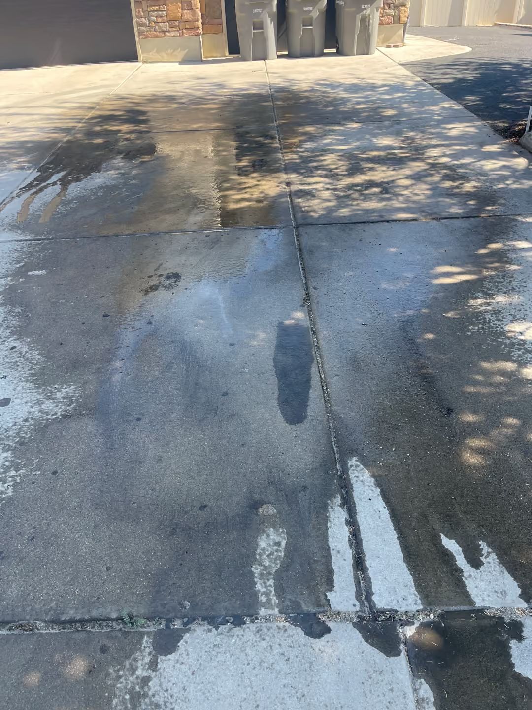 Damaged concrete sidewalk with cracks, water stains, and tree shadows near a curb and building entrance