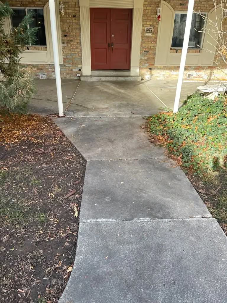 Concrete walkway leading to a red front door with white posts and stone porch columns