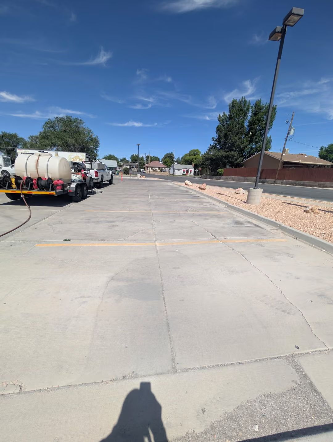 Empty parking lot with parked trucks, a brick wall, and a tall light pole under a clear blue sky