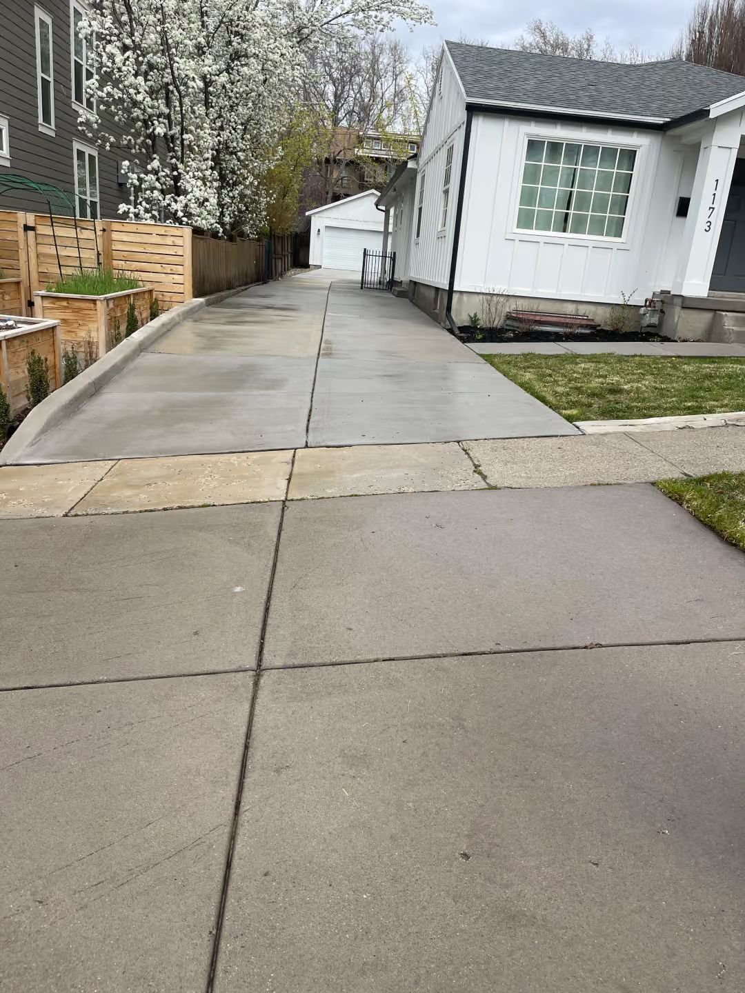 Concrete driveway beside a white house, with a narrow side path and wooden fence on the left.