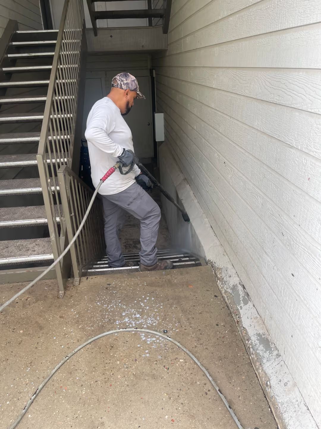 Worker using a pressure washer in a narrow outdoor walkway beside a building