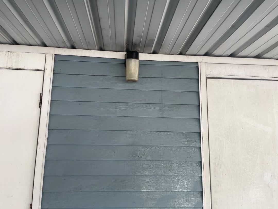 Blue siding wall beneath a corrugated metal roof with a small light fixture centered above.