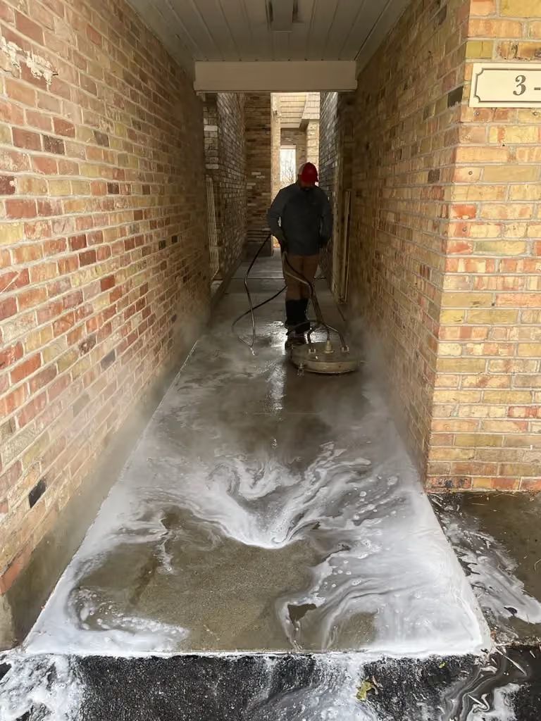 Person washing a brick-lined hallway floor with soap suds and water