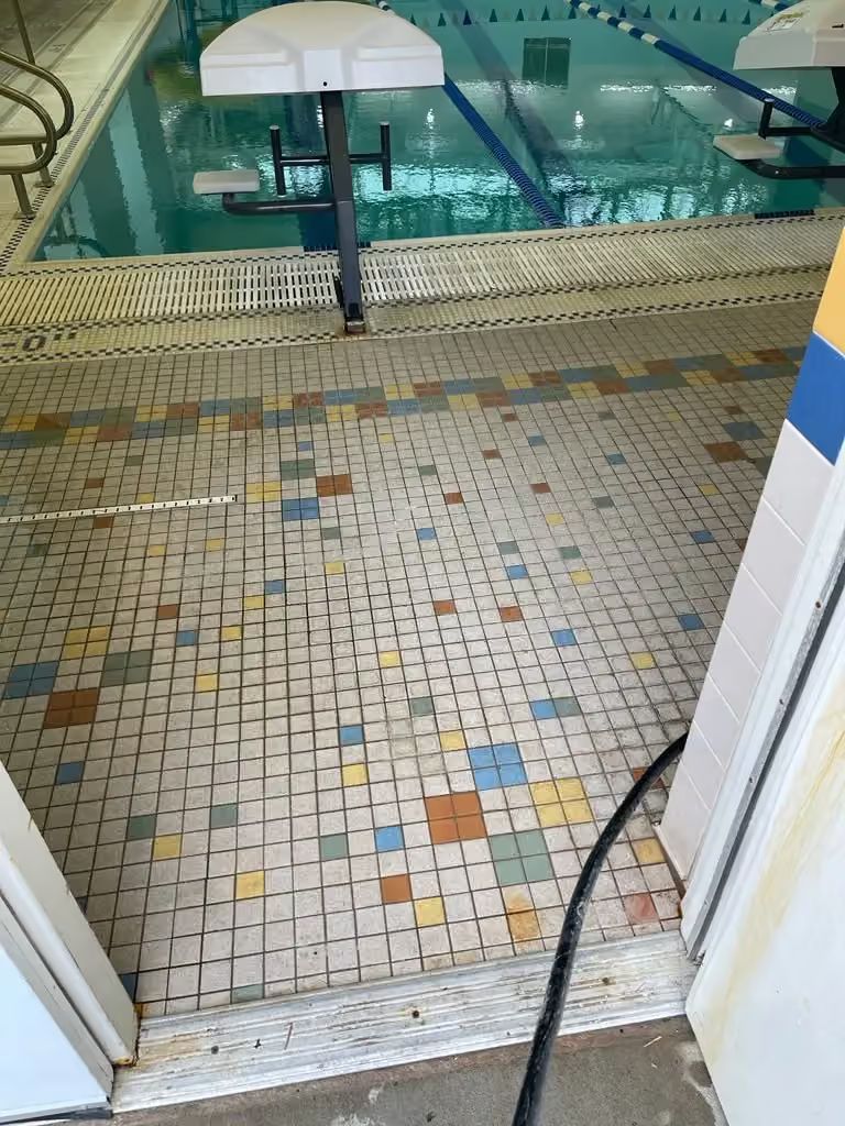Mosaic-tiled walkway beside an indoor pool with turquoise water and a white umbrella stand.