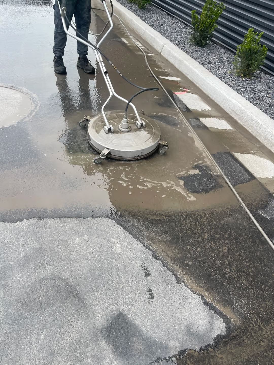 Person pressure-washing a wet parking lot with a circular cleaning tool