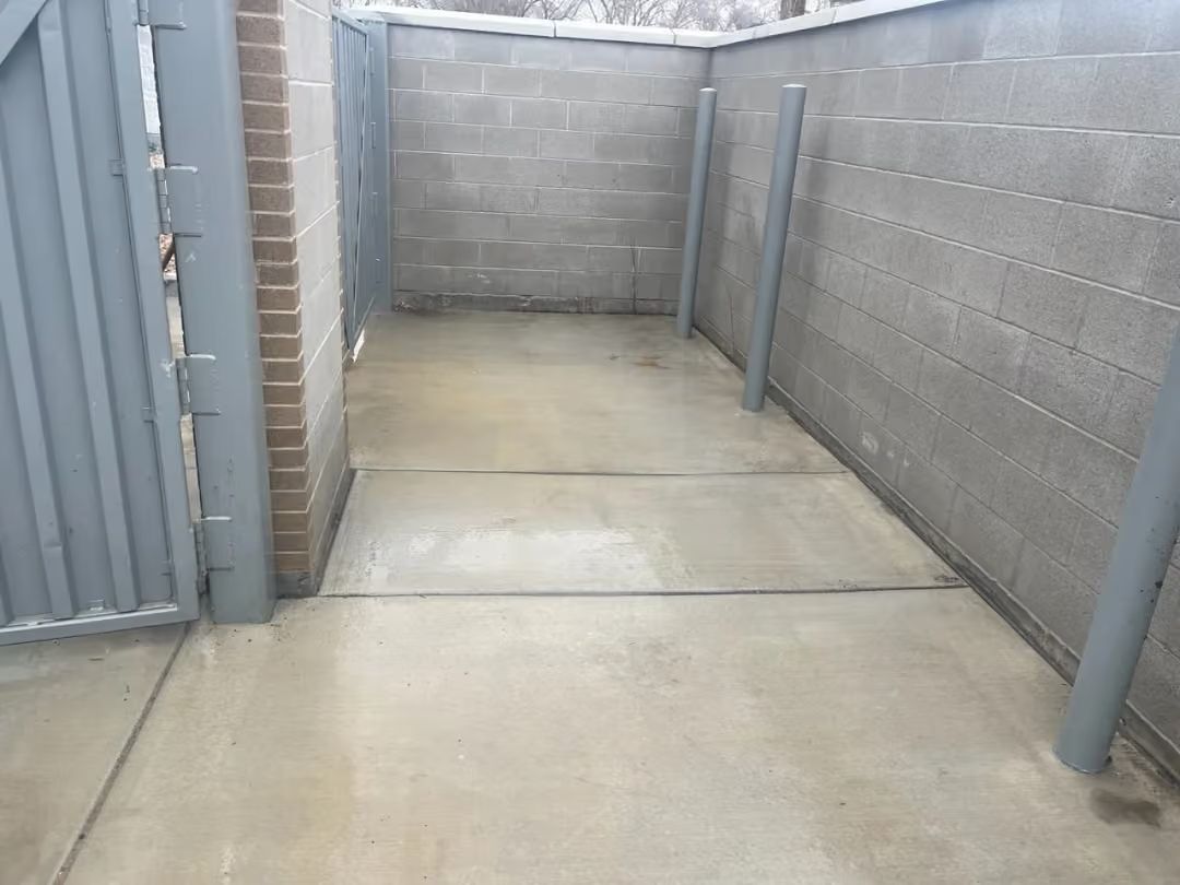 Narrow concrete alley with cinder block walls and gray metal gates on the left.