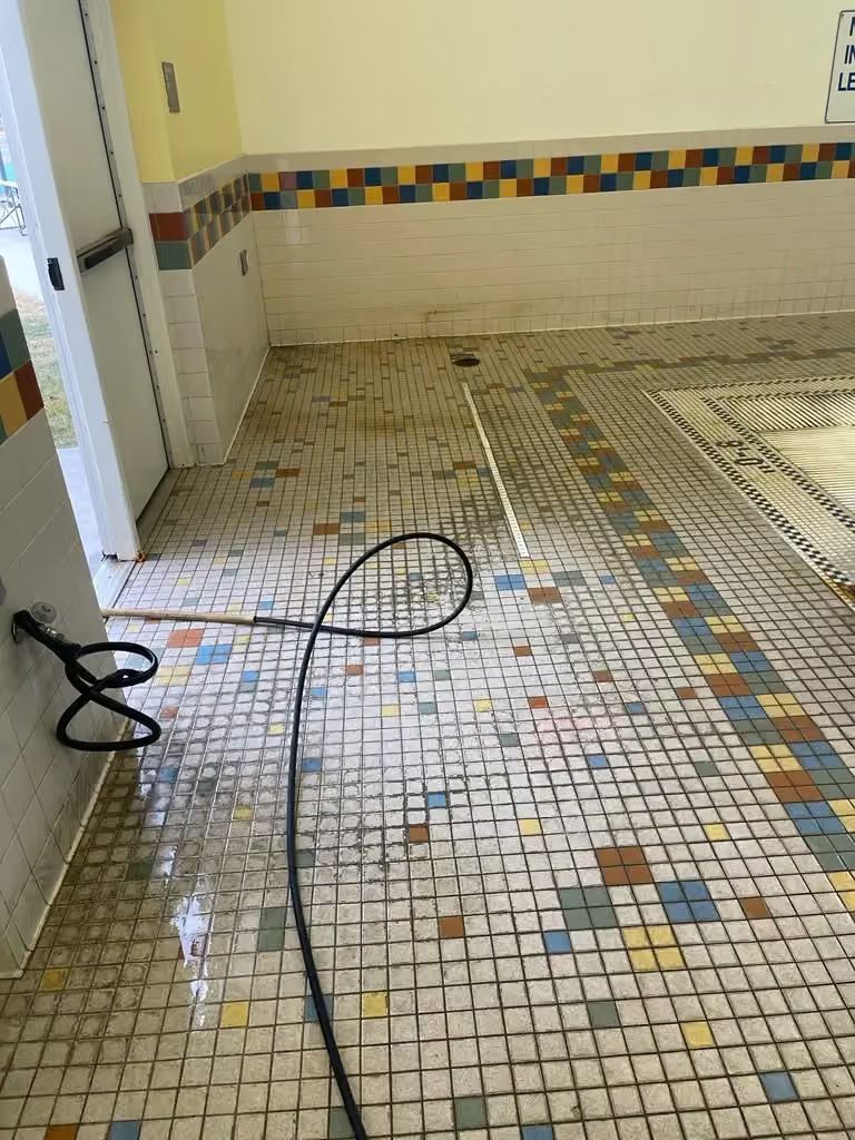 Wet mosaic-tile bathroom floor with a black cable across it and a tiled wall with a colorful border