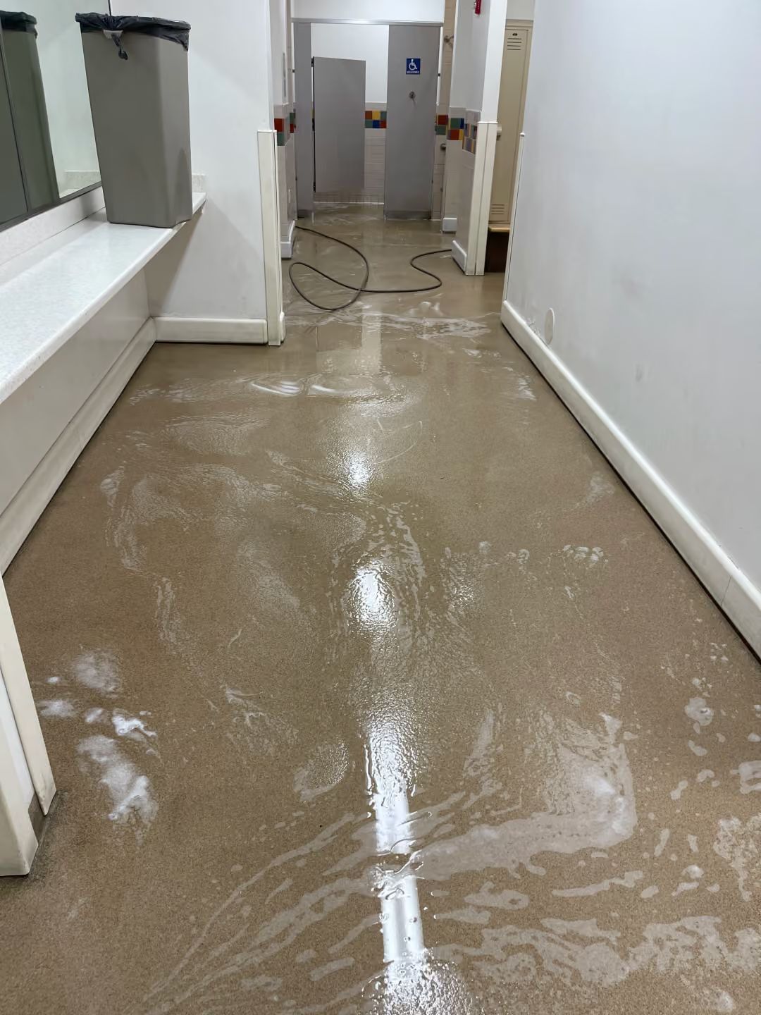 Flooded hallway with muddy water reflecting light, leading to a doorway and utility area.