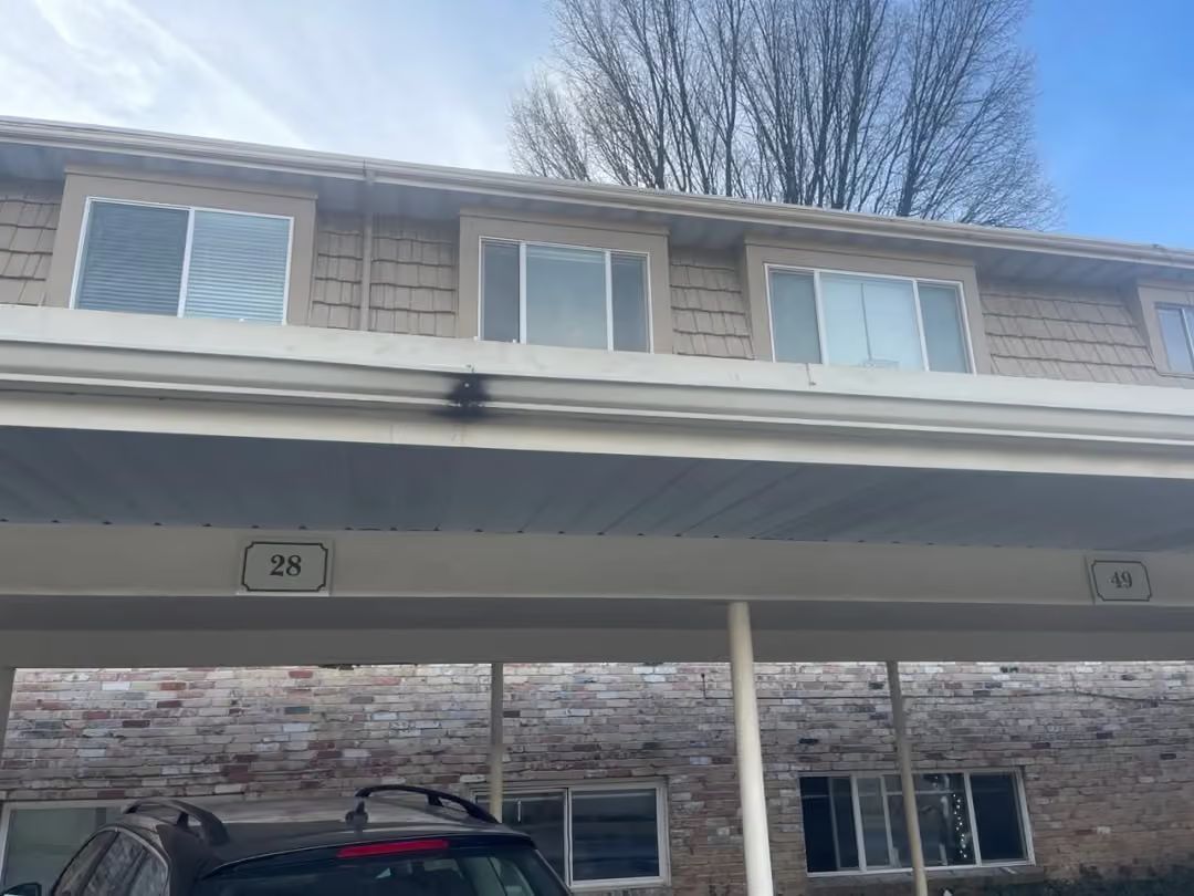 Two-story apartment building with stone lower facade and gray upper siding under a blue sky