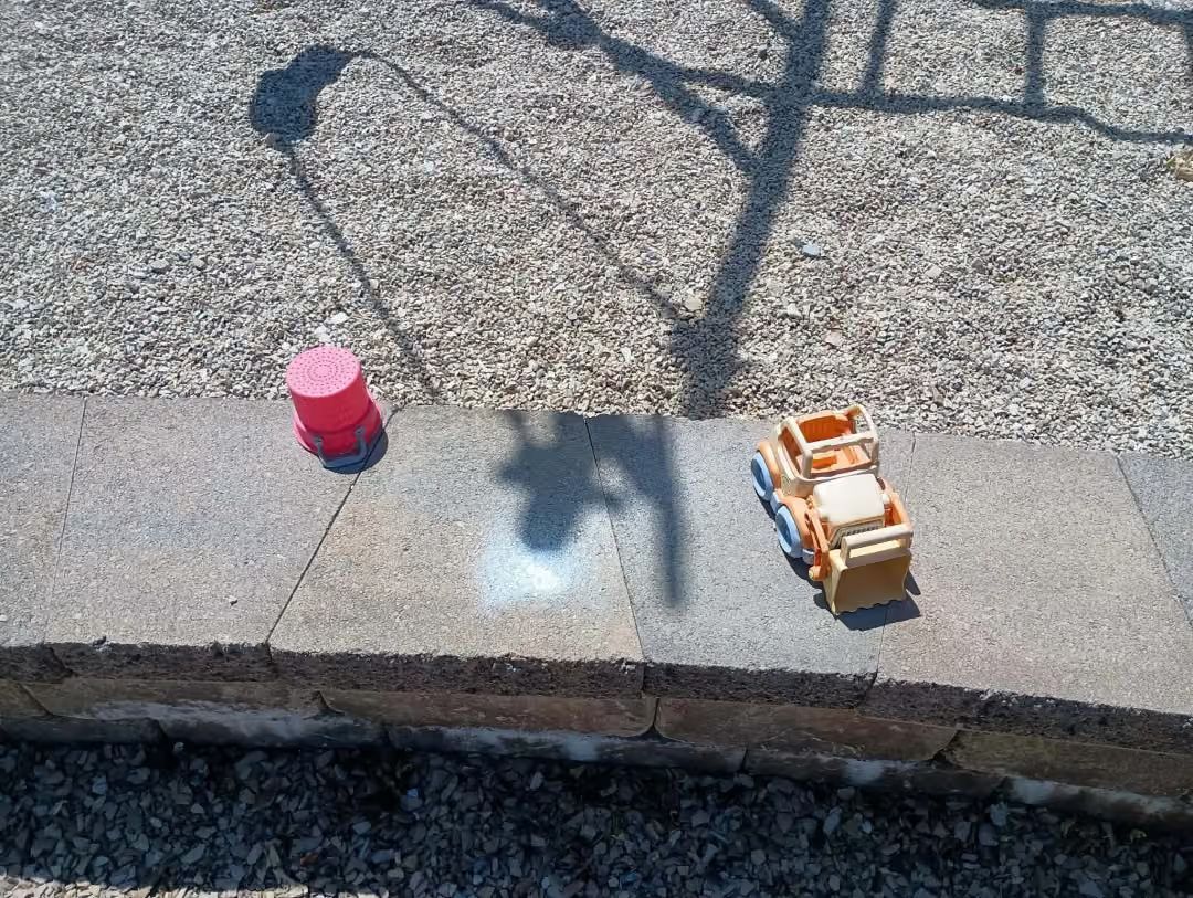 Small pink cup and orange toy car on a concrete ledge in sunlight