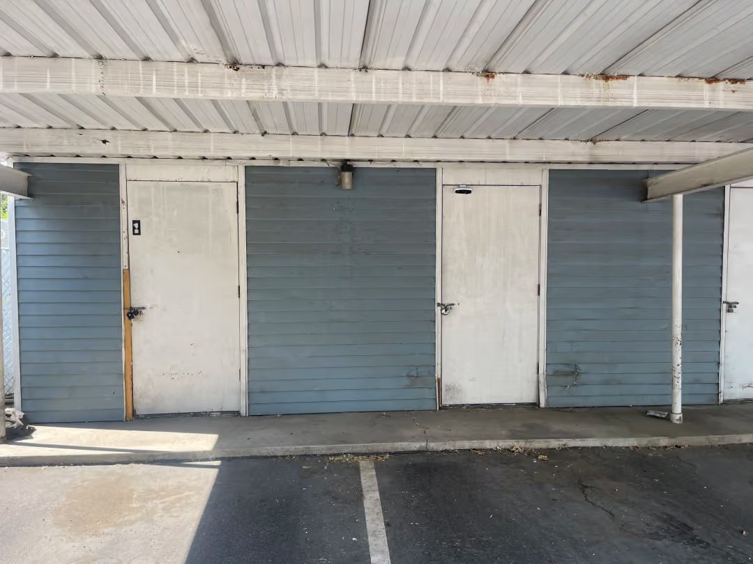 Row of closed blue roll-up garage doors under a white covered awning, with a concrete floor.
