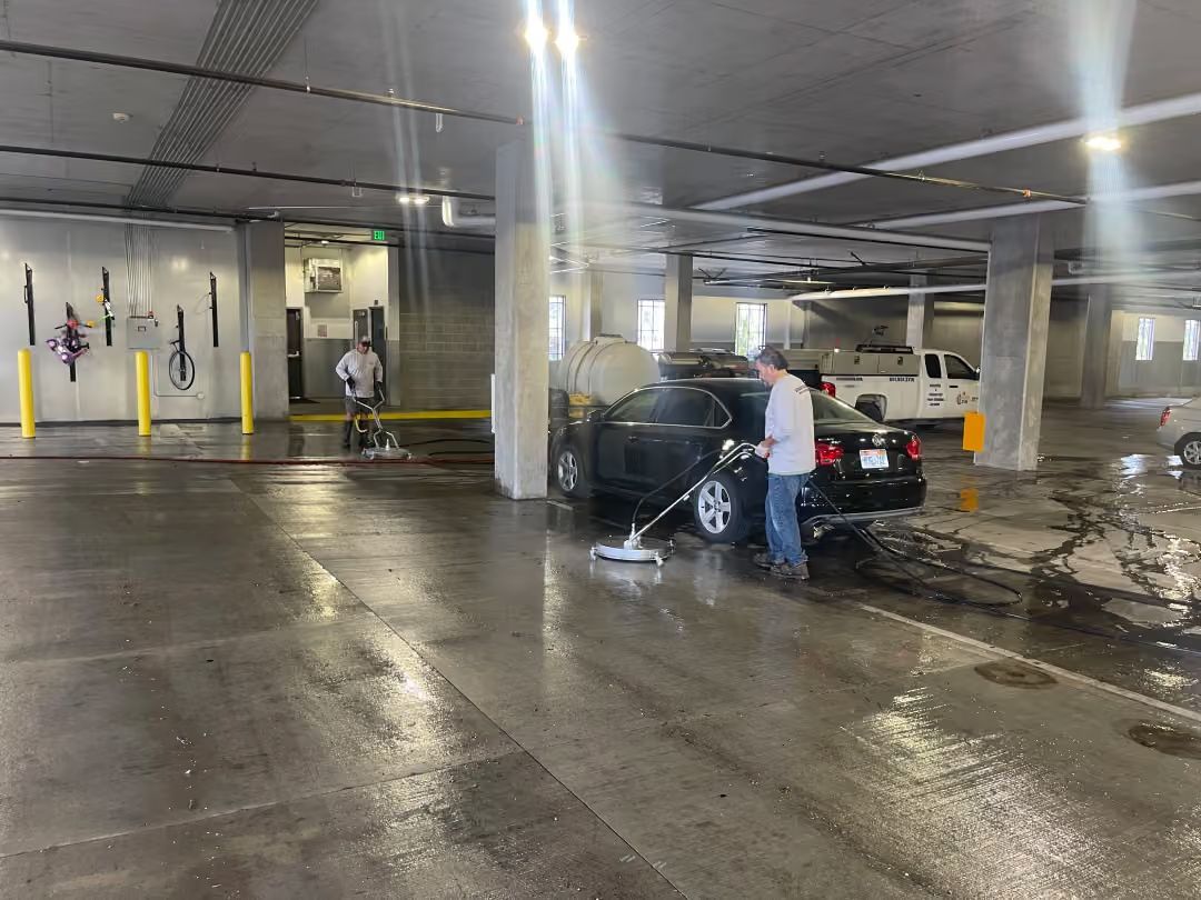 Person washing a black car in a wet parking garage beside a white SUV