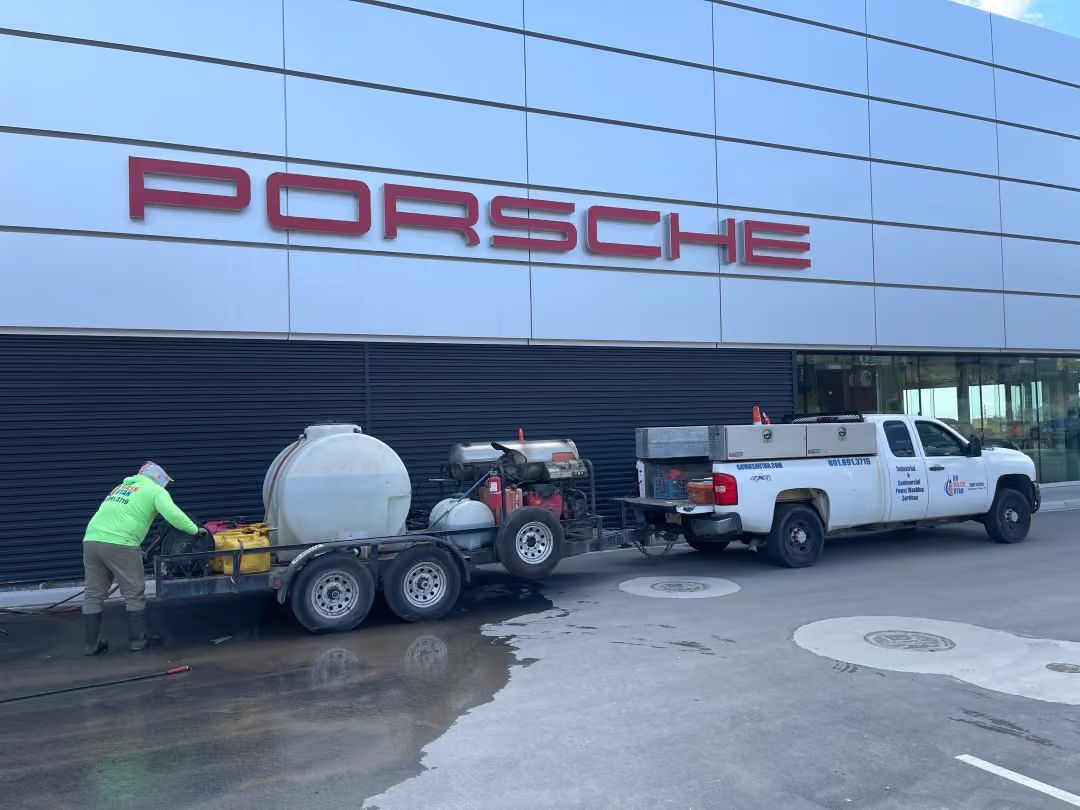 Workers with a trailer and truck outside a Porsche dealership sign