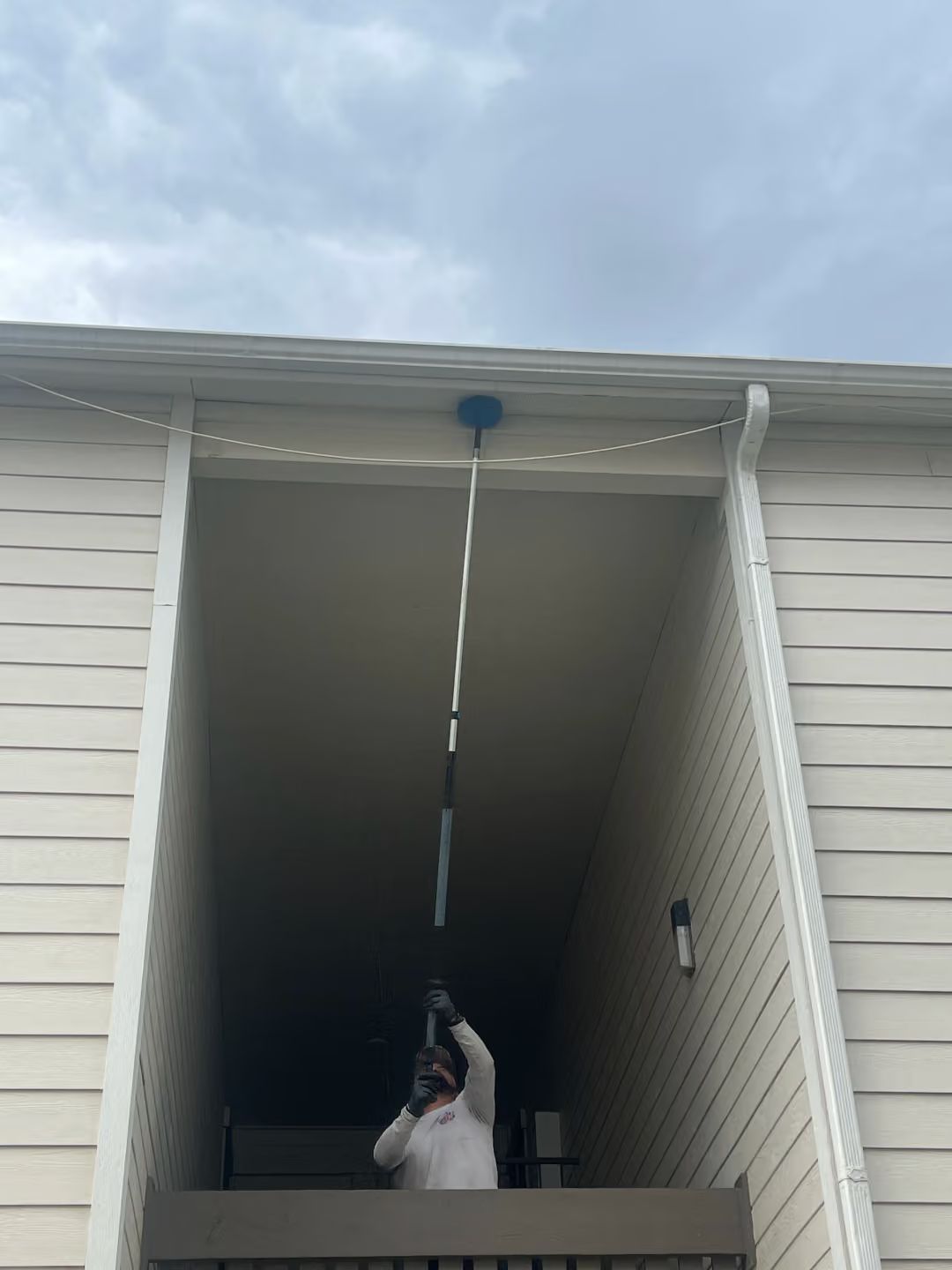 Person in a cat costume reaching up to a blue balloon/string in a covered outdoor entryway.