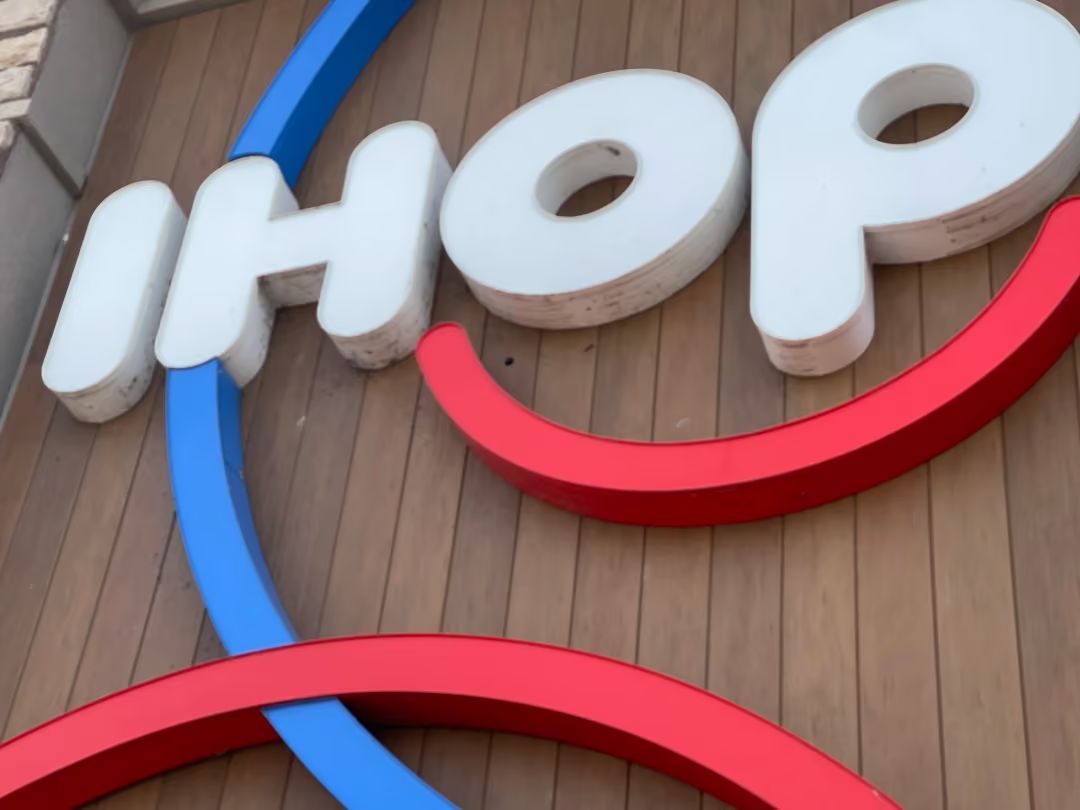 Close-up of the IHOP logo sign with blue and red arcs on a wooden exterior wall