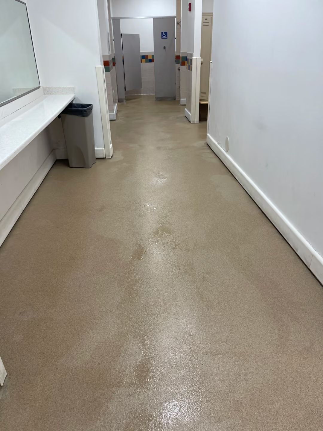 Narrow white hallway with beige floor leading to a doorway at the end.