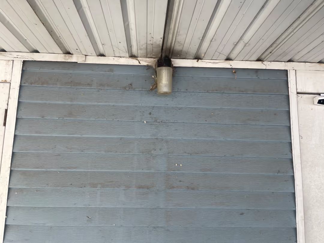 Gray wall beneath a white corrugated roof with a small vent pipe centered above
