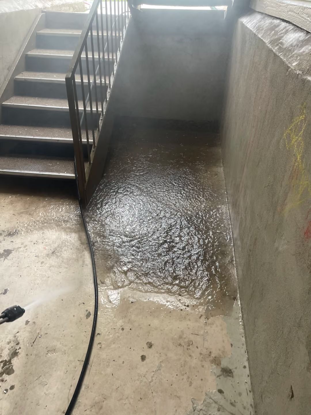 Wet concrete walkway beside stairs and a wall, with water pooled at the bottom.