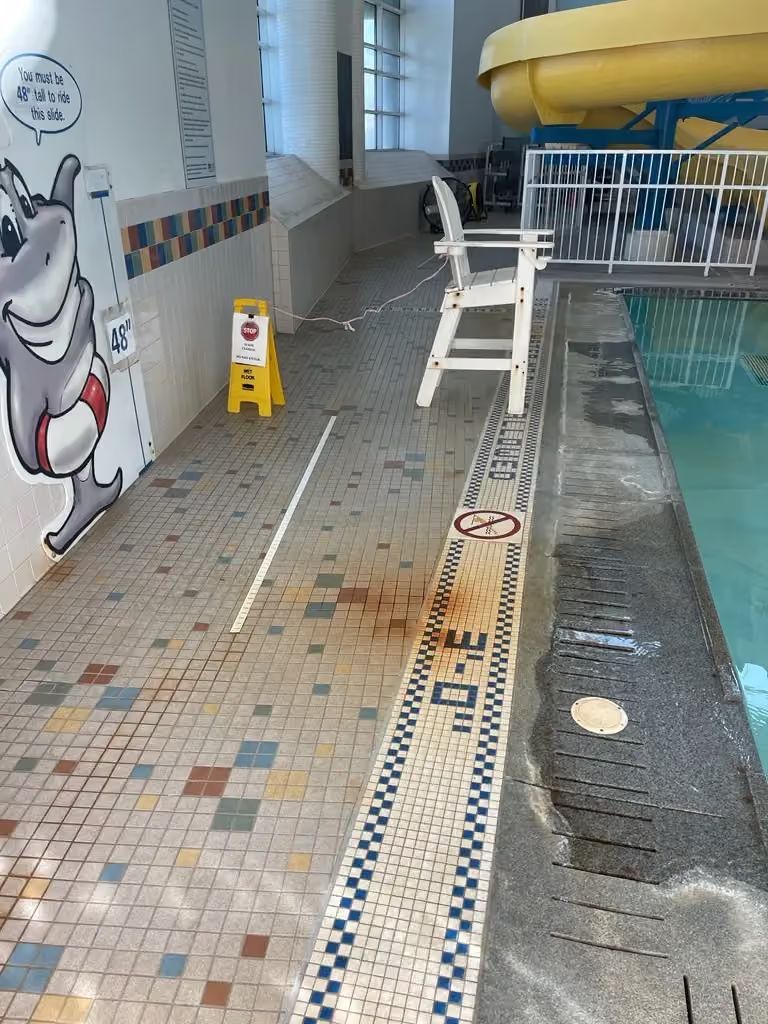 Indoor pool deck with lane markings, diving blocks, and a shallow pool beside a mural wall