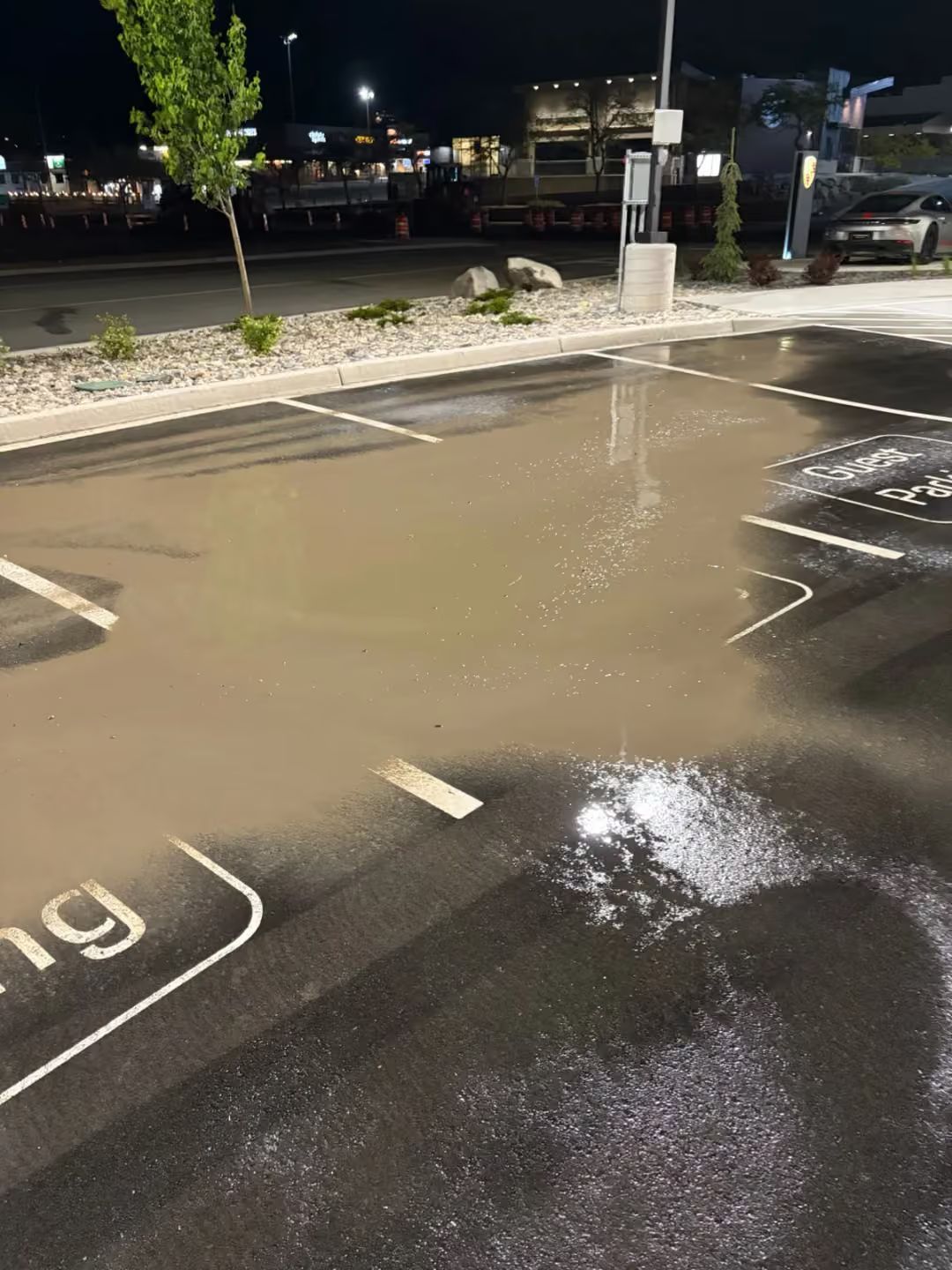 Flooded parking lot at night with standing muddy water reflecting lights