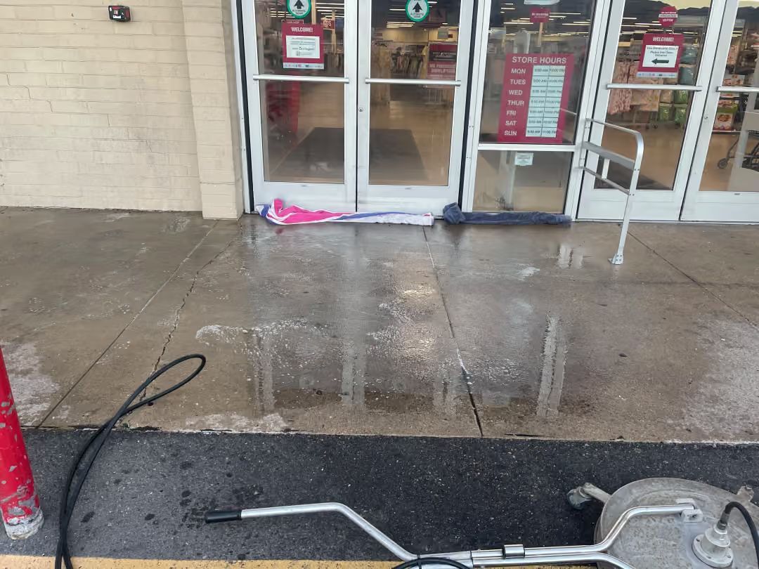 Wet storefront entrance with puddles, glass doors, and a pink item on the ground near the threshold